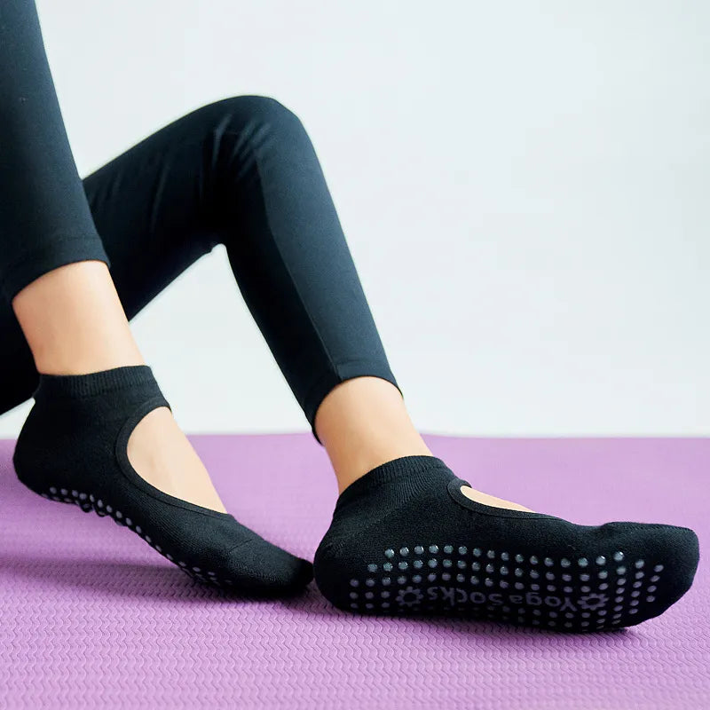 Person wearing black yoga socks on a purple mat with a white background