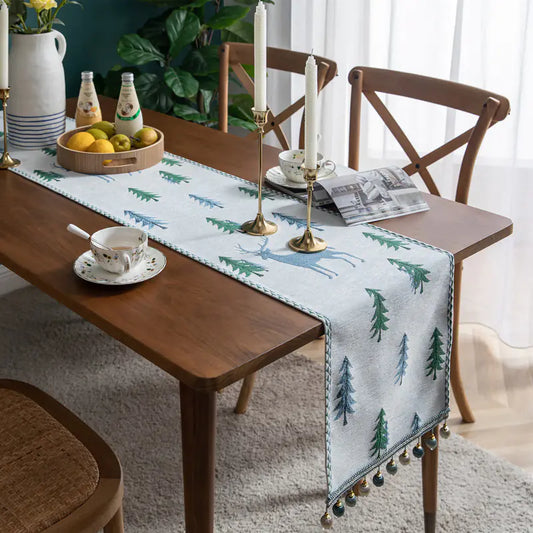 Dining table with a decorative table runner featuring trees and deer, surrounded by chairs and tableware.