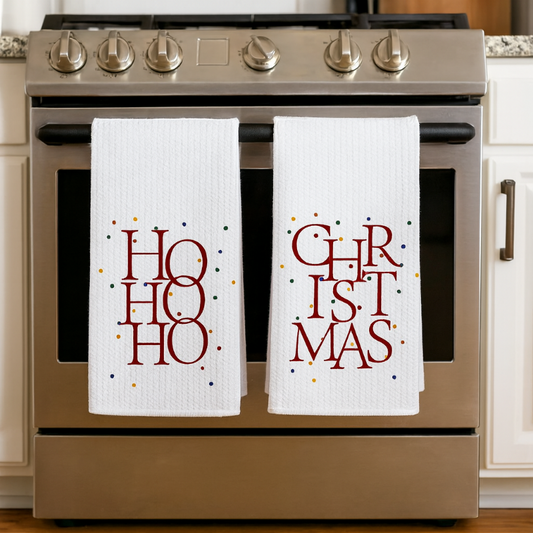 Two Christmas-themed towels hanging on a stove handle.