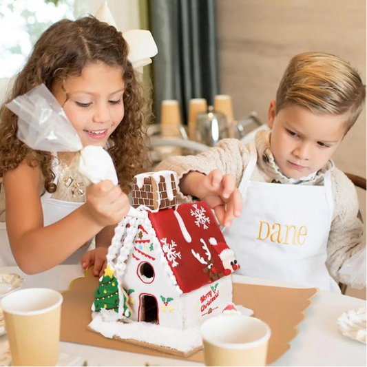 Two children, a girl and a boy, decorating a gingerbread house together.