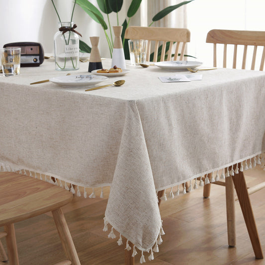 Dining table set with a beige tablecloth, plates, and glasses in a bright room.